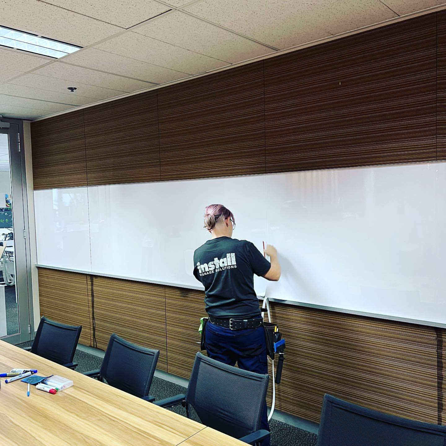 Claire planning an install on a boardroom whiteboard, wearing a branded install tee
