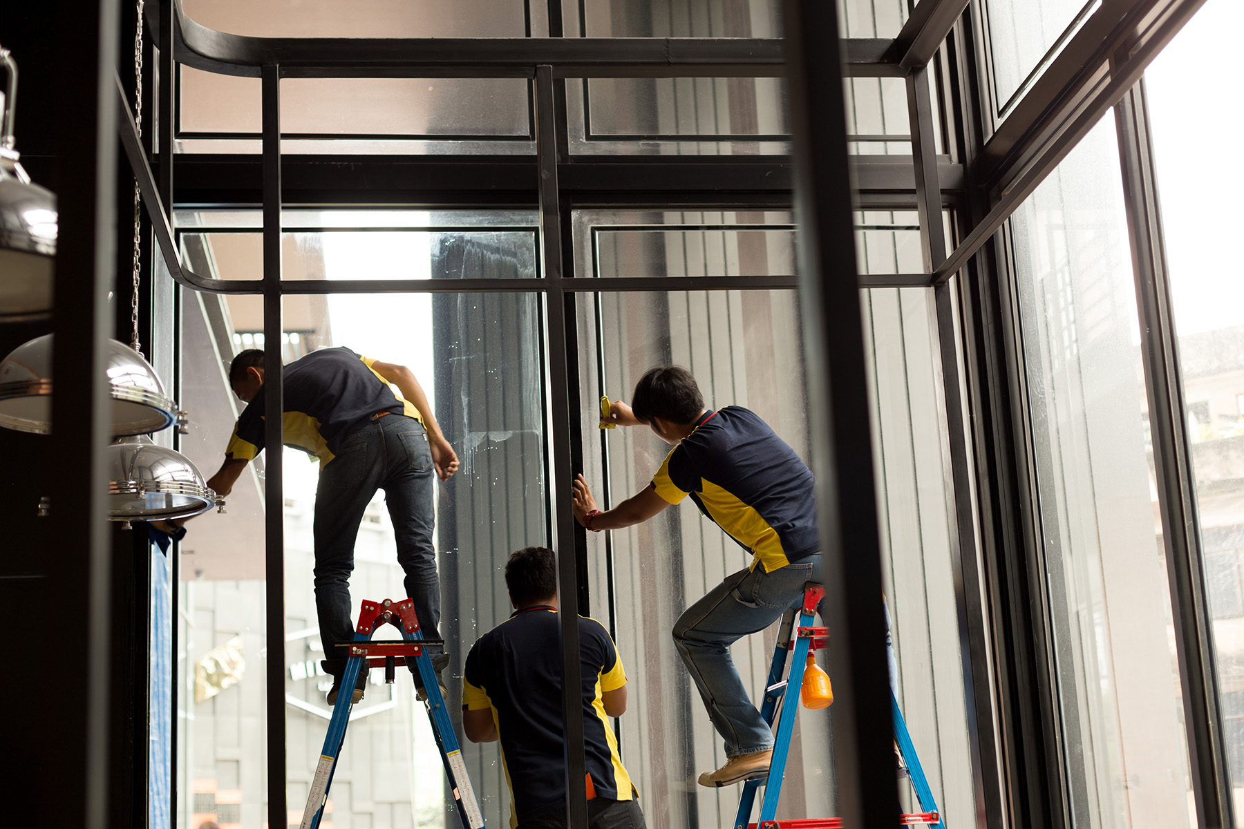 Three-installer team fitting solar tint film across a tall commercial storefront