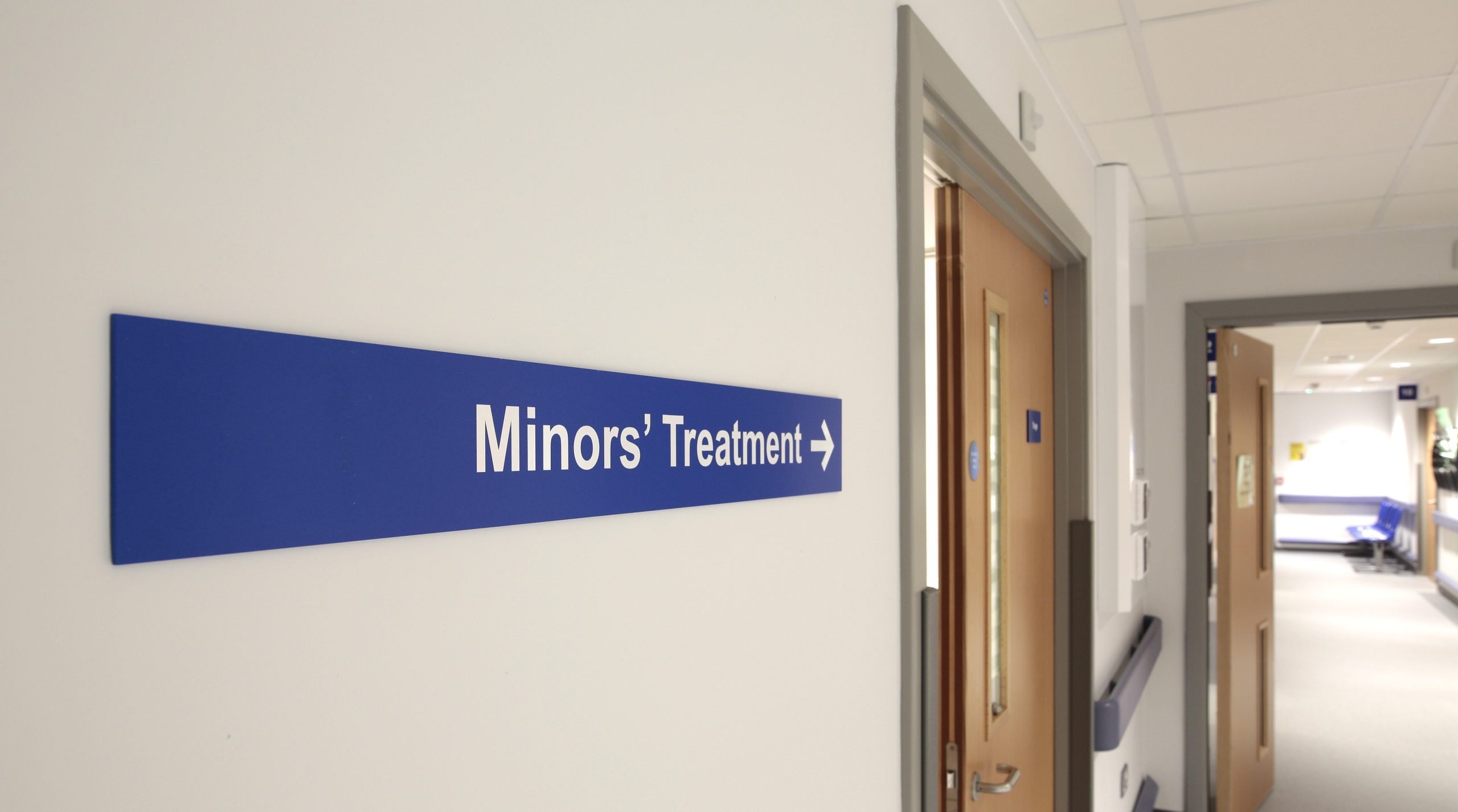 Blue directional wayfinding sign guiding visitors to Minors' Treatment in a hospital corridor