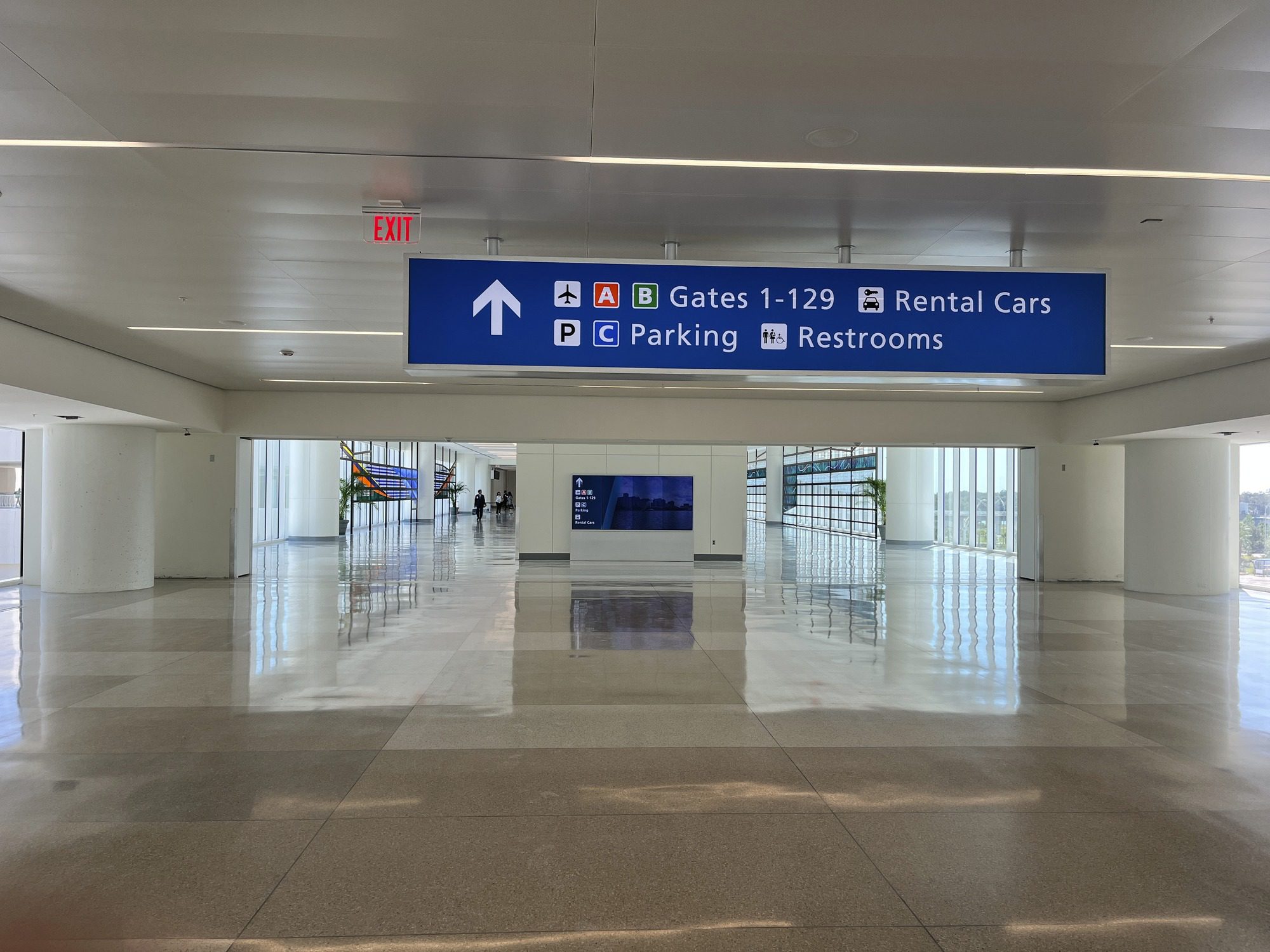 Overhead blue directional signage for gates, parking and rental cars in a transit hall