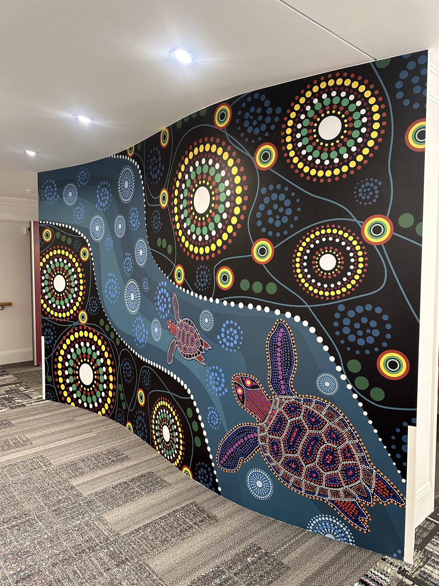 First Nations turtle dot-art mural wrapping around a curved corporate hallway
